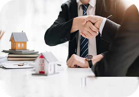 Real estate professionals shaking hands across a desk with model homes
